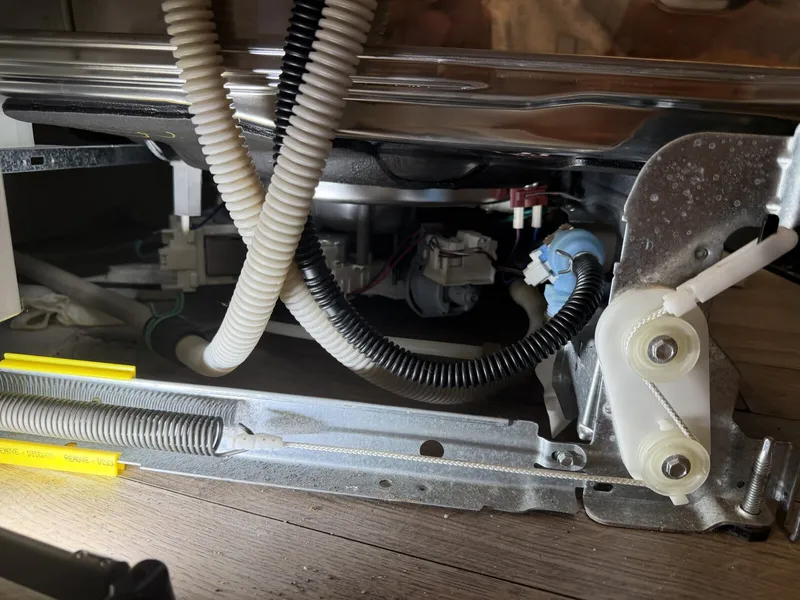 Underside of the dishwasher with hoses, wiring and door spring